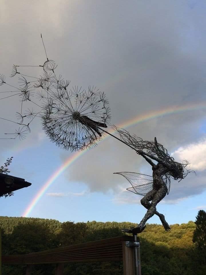 fée en fil de fer; retenant un pissenlit dont les graines s'envolent sous le venre, de l'artiste Robin Wight, sous une lumière dorée